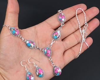 Könnte beinhalten: Ein silbernes Halsketten- und Ohrringset mit tropfenförmigen Einlagen aus einer Mosaik aus rosa, blauen und weißen Steinen. Die Halskette hat einen zentralen Anhänger und eine feine Kette mit Karabinerverschluss. Die Ohrringe haben Silberhaken.