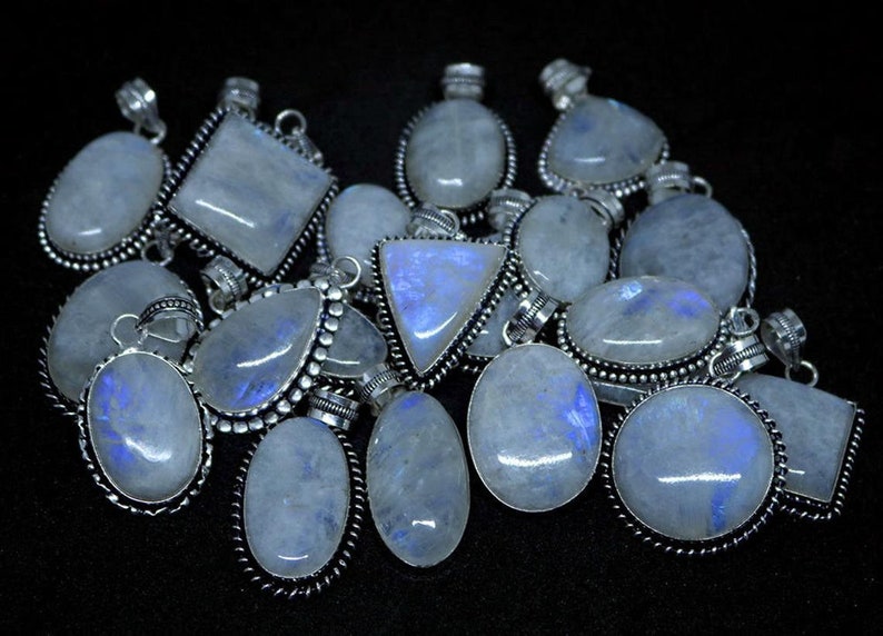 May include: A collection of silver pendants with moonstone gemstones. The pendants are in various shapes, including oval, square, and triangular. The moonstone is a milky white color with a blue iridescent sheen.