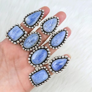 May include: A collection of silver-toned rings with large, light blue gemstones in various shapes, including oval, teardrop, and rectangular. Each ring features a beaded border around the stone. The rings are displayed on a hand.