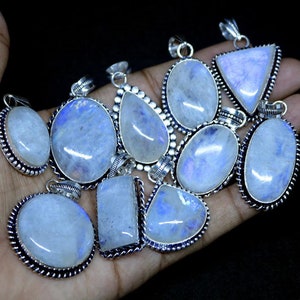 May include: A collection of 12 silver pendants with moonstone gemstones. The pendants are oval, teardrop, and triangular shaped. The moonstone gemstones are iridescent and have a blue and white color.