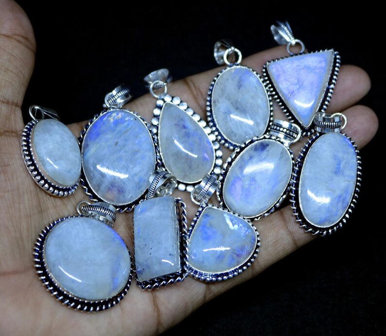 May include: A collection of 12 silver pendants with moonstone gemstones. The pendants are oval, teardrop, and triangular shaped. The moonstone gemstones are iridescent and have a blue and white color.