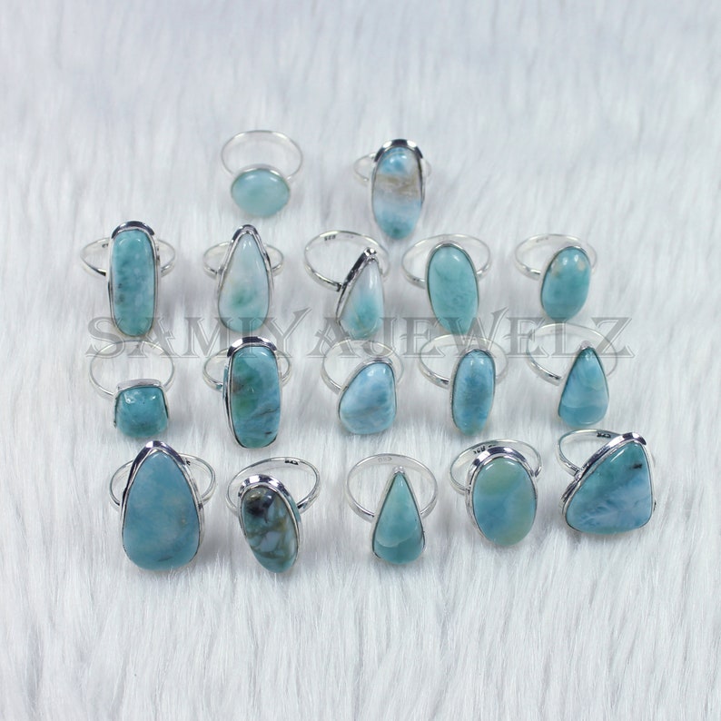 May include: A collection of 16 silver rings with blue-green gemstone settings. The rings feature a variety of shapes and sizes of gemstones, including oval, round, and teardrop.