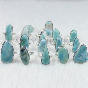 May include: A collection of 15 silver rings with blue and white gemstone settings. The rings are arranged on a white fuzzy surface.