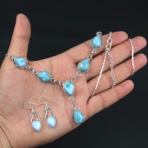 K&ouml;nnte beinhalten: Ein silbernes Halsketten-, Ohrring- und Anh&auml;nger-Set mit hellblauen, tropfenf&ouml;rmigen Edelsteinen. Das Set umfasst eine Halskette mit mehreren Steinen, passende Ohrringe und einen Anh&auml;nger. Der Text "SAMIWJEWELZ" ist sichtbar.