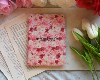 Może przedstawiać: Różowa okładka książki we wzory kwiatowe z napisem "girls just wanna read books" jest otoczona różowymi, białymi i czerwonymi różami i tulipanami. Okładka książki spoczywa na marmurowej powierzchni z otwartymi stronami książki.