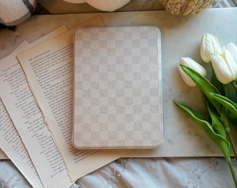 May include: A light gray, checkered pattern tablet case rests on open book pages. Decorative pumpkins in white knit and woven straw are in the background, along with white tulips. The scene is set on a marble surface.