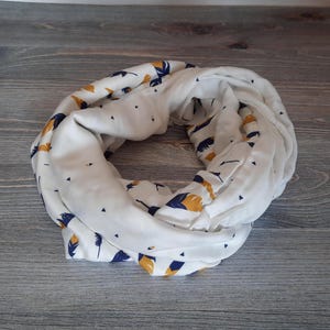 May include: White infinity scarf with a pattern of blue and gold feathers.