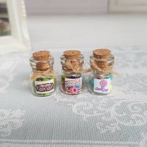 May include: Three small glass jars with cork lids and twine tied around the necks. Each jar is filled with colourful candy and has a label that says "Candy Shop".