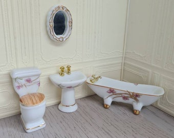 Pode incluir: Um conjunto de banheiro de porcelana em miniatura com um vaso sanitário, uma pia e uma banheira brancos. Cada peça apresenta um design floral com flores rosa e detalhes dourados.