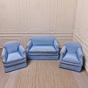 May include: A set of three miniature blue striped furniture pieces, including a loveseat and two armchairs. The furniture is made of a light blue fabric with white stripes and is sitting on a wooden floor.