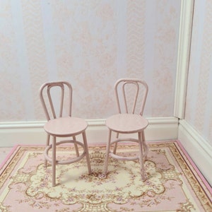May include: Two pink metal chairs with a floral patterned rug underneath. The chairs have a simple design with a curved back and a round seat.