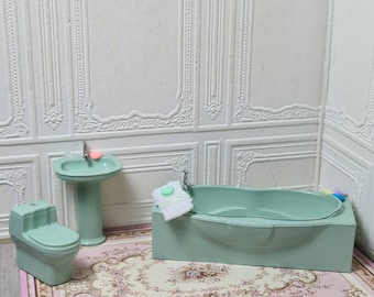 May include: A miniature bathroom set with a green toilet, sink, and bathtub. The set is on a pink and cream floral rug.