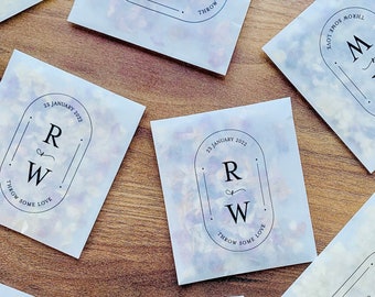 May include: A collection of white paper bags with a light blue watercolor background. Each bag has a black and white design with the initials "R & W" and the text "Throw some love" and the date "23 January 2022".
