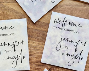 May include: Four white paper bags with a watercolor effect and black text. The text on the bags reads "Welcome to the wedding of Jennifer & Angelo".