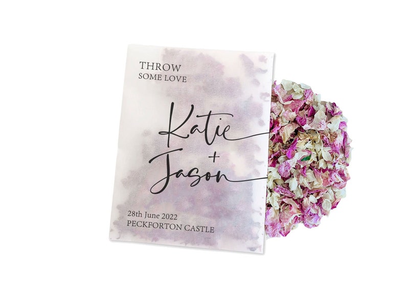 May include: White paper bag with the text "THROW SOME LOVE" and "Katie + Jason" in black script. The date "28th June 2022" and "PECKFORTON CASTLE" are also printed on the bag. The bag is filled with pink and white flower petals.