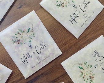 May include: White paper favor bags with a floral design and the text "Matt + Callie" and "Marylebone Town Hall" printed on them. The bags are for a wedding.