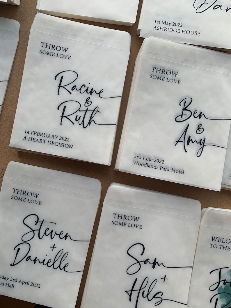 May include: White paper bags with black calligraphy text. The bags have the text "Throw some love" and the names of couples getting married. The text includes the date and location of the wedding.