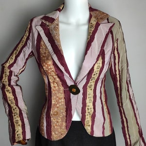 May include: A striped blazer with a pink, burgundy, and gold color scheme. The blazer has a single button closure and a pointed collar.