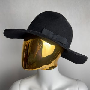 Puede incluir: Un sombrero de fieltro negro de ala ancha con un lazo de grosgrain negro.