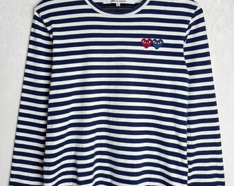 May include: A long-sleeved, striped shirt in navy blue and white. The shirt features three heart-shaped graphic designs in red and blue on the chest. The brand name "PLAY" is visible on the label.