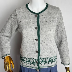 May include: A gray cardigan with a green trim and buttons. The sweater has a speckled pattern and a green and white geometric design at the bottom. The cardigan is displayed on a mannequin.
