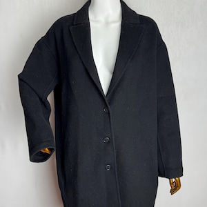 May include: A black wool coat with a classic lapel collar and three-button closure. The coat has long sleeves and a relaxed fit, suitable for layering. The coat is displayed on a mannequin.