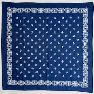 May include: A square blue bandana featuring a white floral border pattern and a repeating small white floral motif across the centre. The fabric includes the printed text 100% BAUMWOLLE/COTTON/COTON in the bottom right corner of the design.