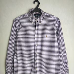 Può includere: Una camicia a maniche lunghe con bottoni e un motivo a quadri vichy bianco e viola. La camicia ha un piccolo logo ricamato di un giocatore di polo sul petto sinistro.