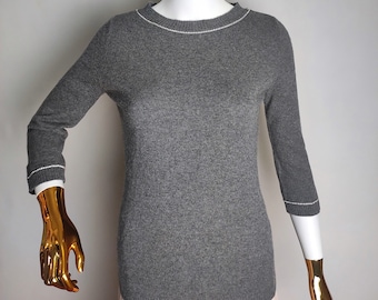 Könnte beinhalten: Ein grauer Pullover mit weißem Besatz an Ausschnitt und Ärmeln. Der Pullover befindet sich auf einer Schaufensterpuppe.