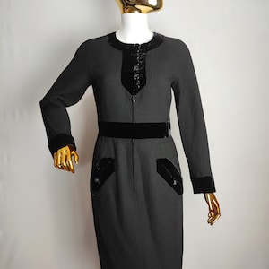 K&ouml;nnte beinhalten: Ein schwarzes Kleid mit Samtbesatz an Ausschnitt, &Auml;rmeln und Taille. Das Kleid hat eine figurbetonte Silhouette und eine knielange L&auml;nge.