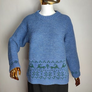 May include: A blue knitted jumper with a green reindeer pattern around the bottom hem.