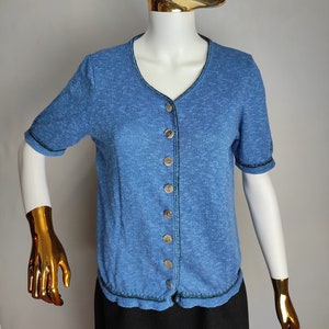 May include: A blue short-sleeved button-up cardigan with a dark green trim. The cardigan is made of a soft, textured fabric.