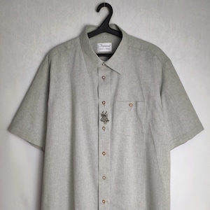May include: Pale green short-sleeved shirt with a button-down front and a chest pocket. The shirt has a deer emblem and the text "Imperial" on the label. It is hanging on a black hanger.
