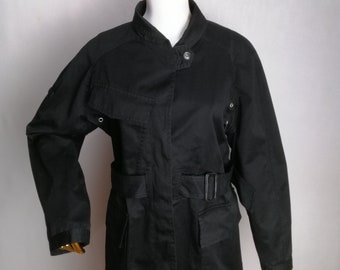 May include: A black utility jacket with a belted waist, multiple pockets, and a stand-up collar.