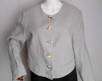 Puede incluir: Una chaqueta de lino gris claro con cuello redondo y cinco botones. Los botones son de material natural y tienen un color marrón claro.