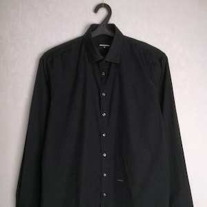 May include: A black long-sleeved button-down shirt with a collar. The shirt has a small logo on the bottom left side.