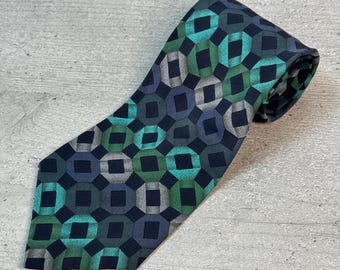 Puede incluir: Una corbata azul marino con un patrón geométrico de formas entrelazadas en tonos de verde azulado, verde y gris. La corbata está hecha de una tela suave y es adecuada para vestimenta formal o de negocios.