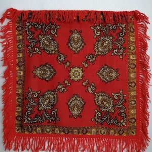 K&ouml;nnte beinhalten: Ein roter quadratischer Schal mit Paisley-Muster und Fransenbesatz. Das Muster ist in Braun- und Goldt&ouml;nen gehalten.