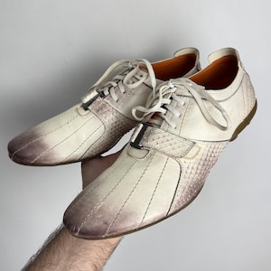 K&ouml;nnte beinhalten: Cremefarbene Ledersneaker mit strukturierten Zehen- und Seitenteilen. Die Schuhe haben einen Schn&uuml;rverschluss, einen schwarzen Akzent und eine braune Sohle. Das Innenfutter ist orange.