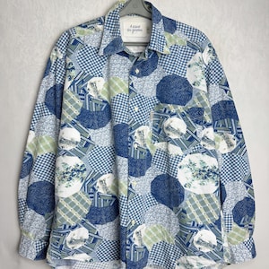 Può includere: Una camicia a maniche lunghe con un design patchwork nei toni del blu, bianco e verde. La camicia presenta un mix di motivi, tra cui quadretti, floreali e forme geometriche. Il testo "A cause des garcons" è visibile sul colletto.