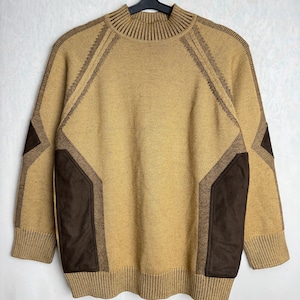 Pode incluir: Um suéter bege com detalhes geométricos e patches marrons. O suéter tem gola, punhos e bainha canelados. O design inclui padrões geométricos marrons nos ombros e patches marrons nos cotovelos.