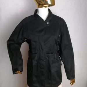 May include: A black utility jacket with a belted waist, multiple pockets, and a stand-up collar.