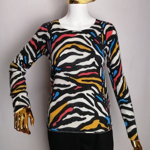 May include: A black and white zebra print sweater with yellow, red, and blue accents. The sweater has long sleeves and a round neckline.