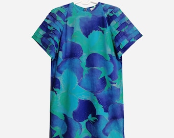Puede incluir: Un vestido de estampado floral azul y verde con mangas cortas y un detalle fruncido en los hombros. El vestido tiene un escote redondo y una silueta recta.