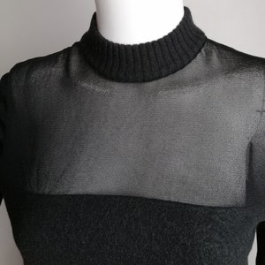 以下が含まれることがあります： 胸元に透けるメッシュパネルが付いた、黒のモックネックセーターです。