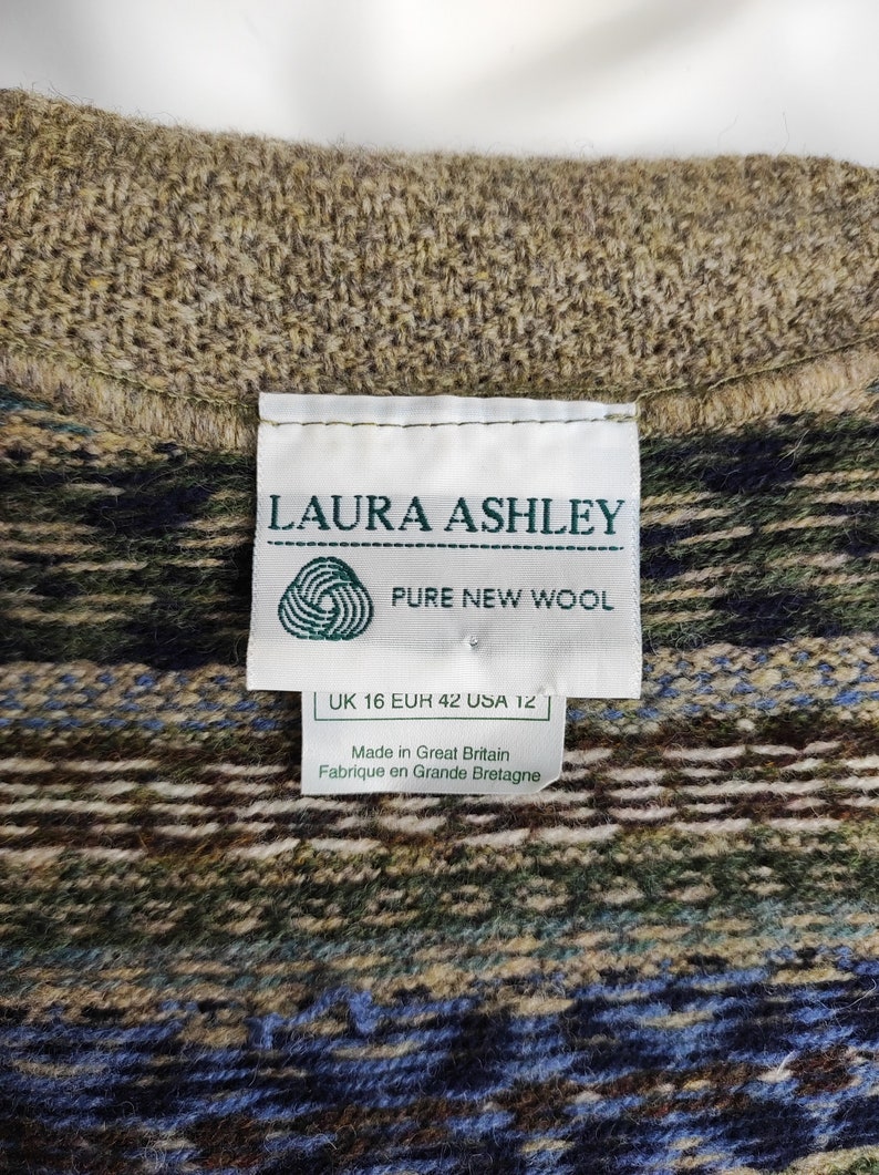 May include: Close-up of a textured wool garment with a patterned design in shades of brown, green, and blue. A white label reads "LAURA ASHLEY PURE NEW WOOL" with size information. Made in Great Britain.