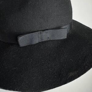 Puede incluir: Un sombrero de fieltro negro de ala ancha con una cinta de grosgrain negra y un lazo.