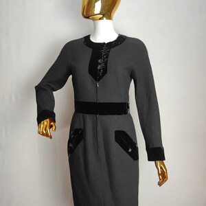 K&ouml;nnte beinhalten: Ein schwarzes Kleid mit Samtbesatz an Ausschnitt, Taille und &Auml;rmelb&uuml;ndchen. Das Kleid hat einen Rei&szlig;verschluss und zwei Taschen mit Samtbesatz.