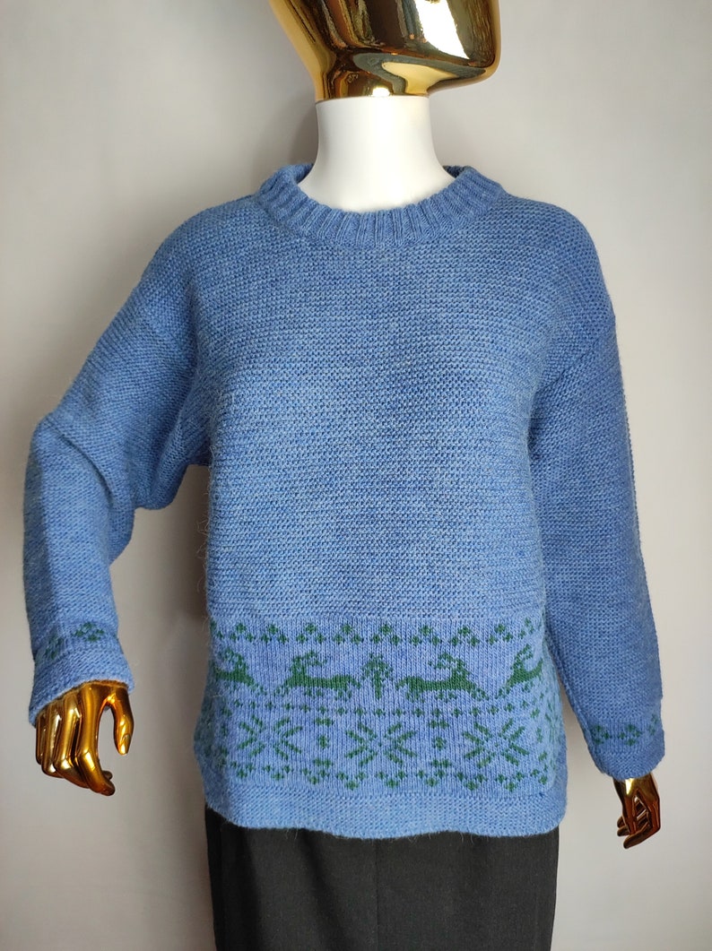 May include: A blue knitted jumper with a green and blue patterned design around the bottom hem.