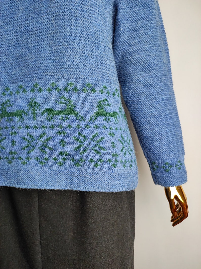 May include: A blue knitted jumper with a green reindeer and snowflake pattern around the bottom.